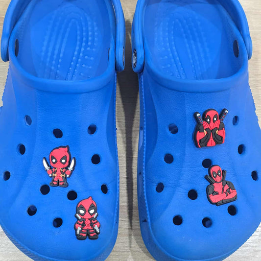 Blue clogs with Deadpool character stickers on a light wooden surface