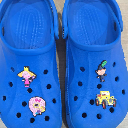 Blue children's clogs with cartoon character pins on a wooden floor.