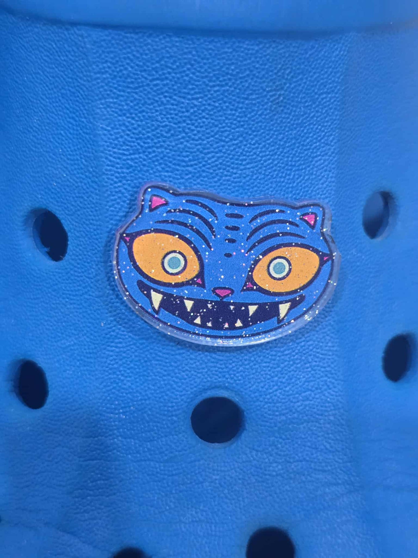 Blue croc with a colorful cat face patch on a blue background