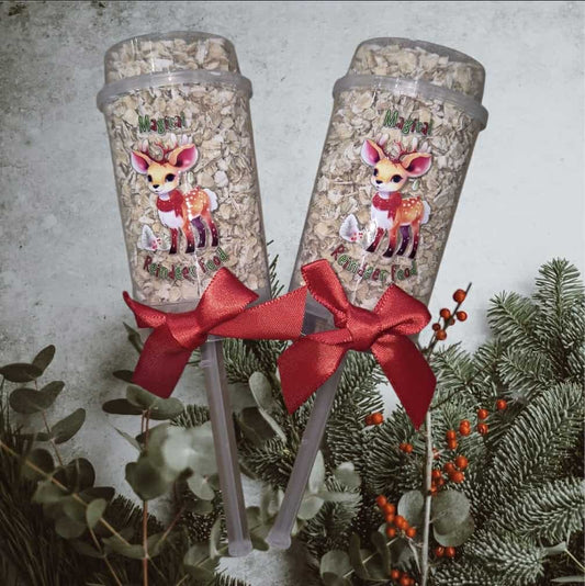 Two tumblers with deer designs and red bows, surrounded by greenery on a light background