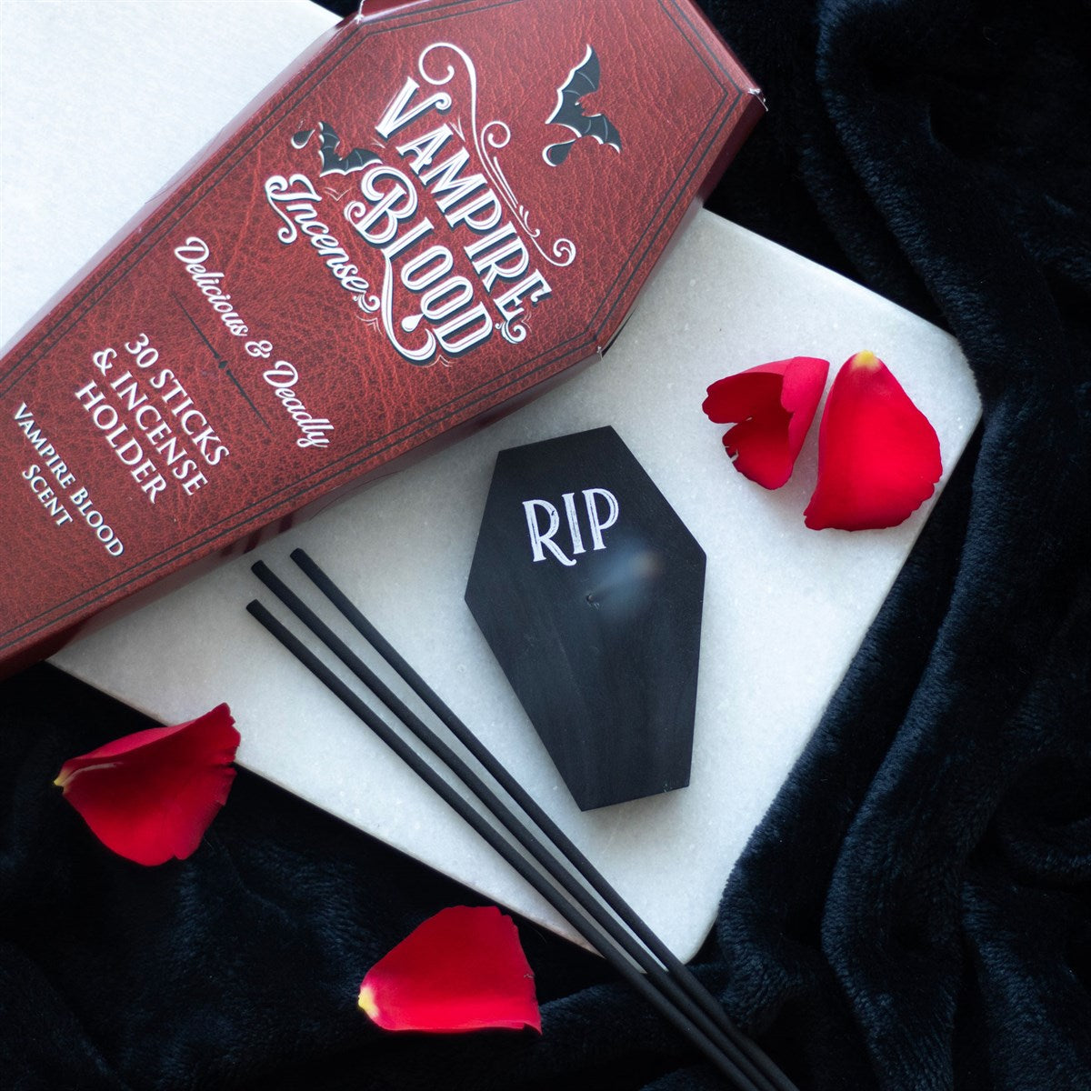 Vampire Bloody product with coffin-shaped incense holder and red rose petals on a dark surface.