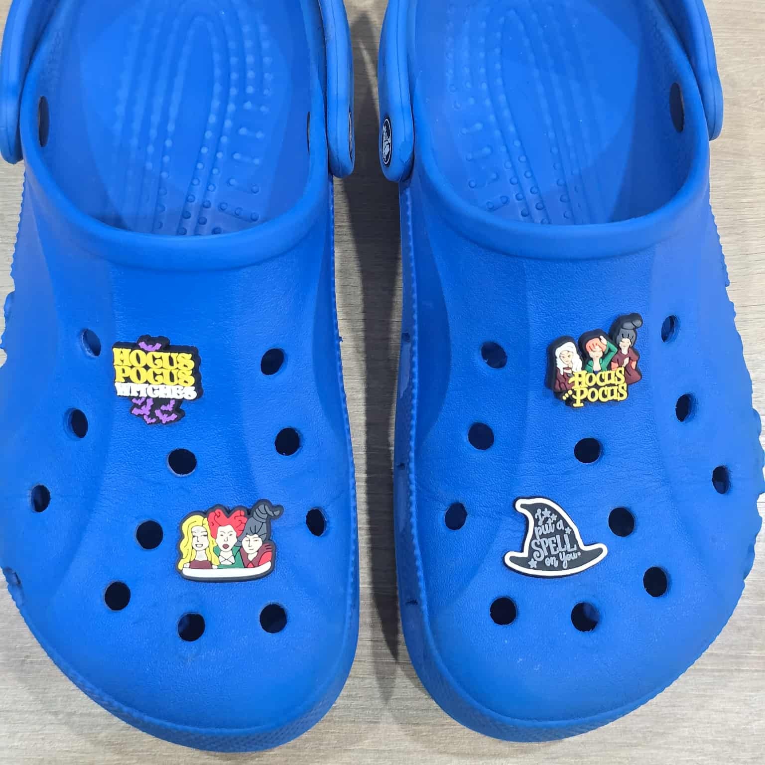 Pair of blue clogs with cartoon character stickers on a light wooden surface