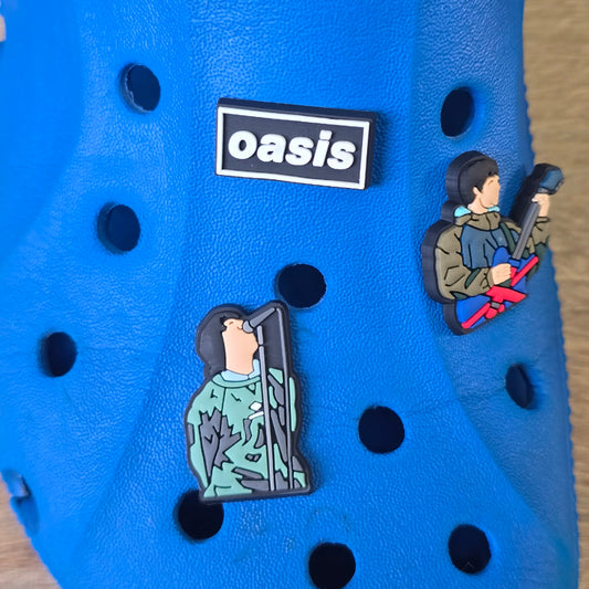 Blue shoe with 'oasis' logo and character pins on a wooden surface