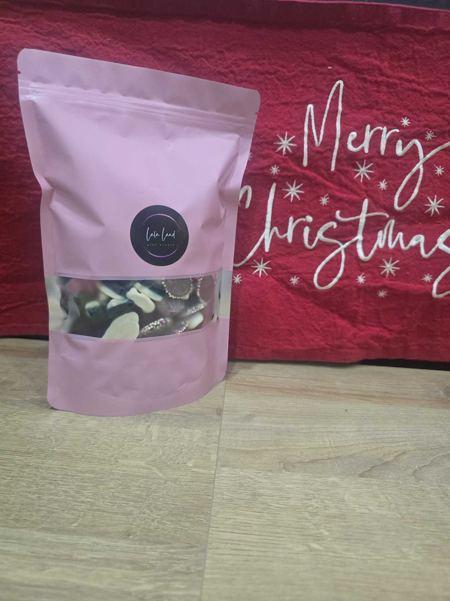 Pink packaging of a product with a visible brand logo on a red 'Merry Christmas' background.